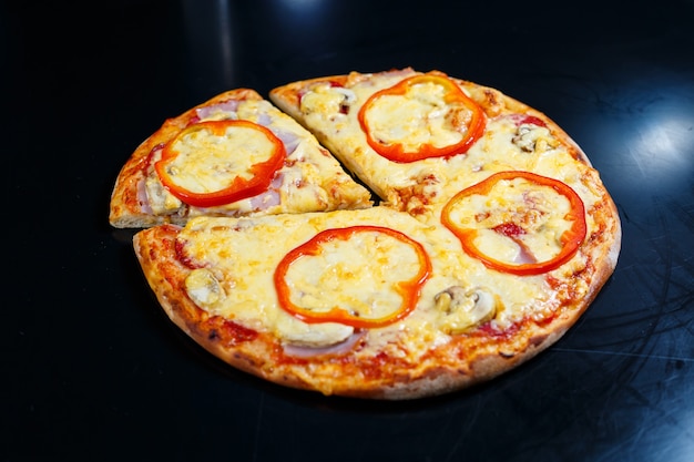 Pizza americana fatta in casa deliziosa calda con pepe rosso e carne con una crosta spessa su un tavolo nero