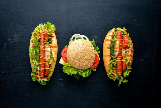 Hot dog and hamburger with cheese, meat and greens on Wooden background. Top view. Free space.