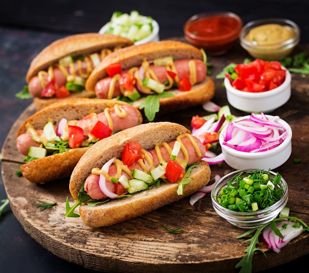 Hot dog with cucumber, tomato and red onion on wooden background.