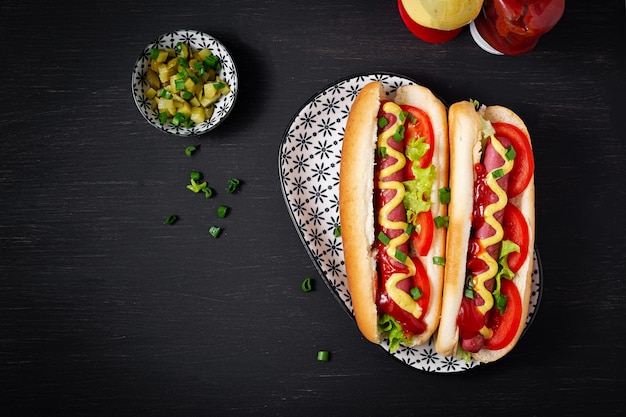 Hot dog with grilled sausage tomato and lettuce on dark background American hotdog Top view overhead