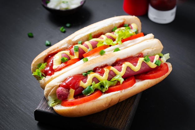 Hot dog with grilled sausage tomato and lettuce on dark background American hotdog