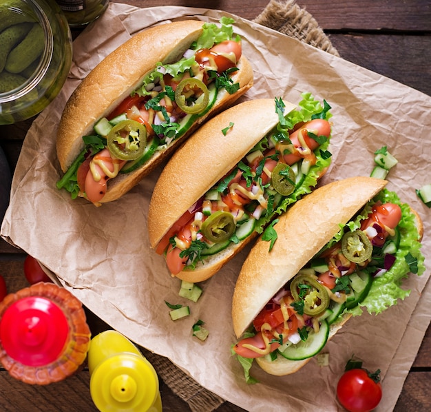 Hot dog with jalapeno peppers, tomato, cucumber and lettuce on wooden surface