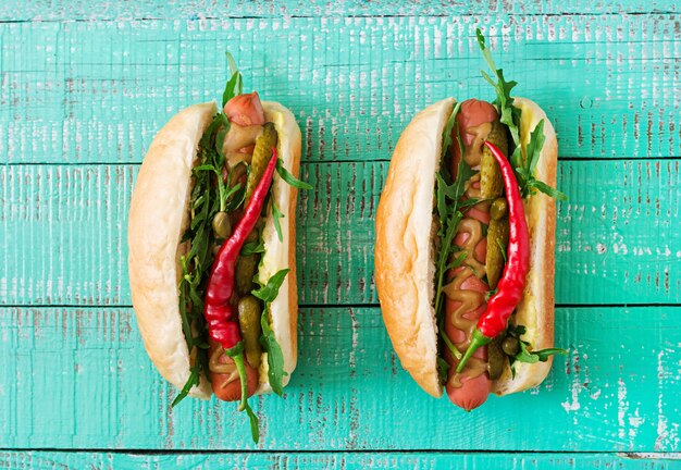 Hot dog con sottaceti, capperi e rucola sul tavolo di legno.