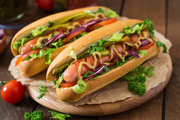 Hot dog with  pickles, tomato and lettuce on wooden surface