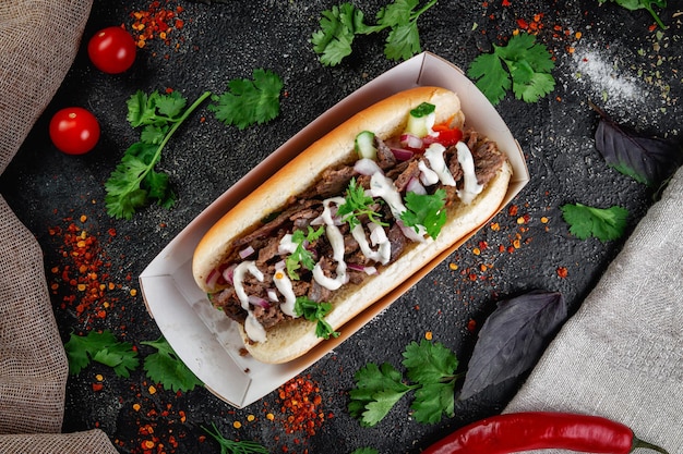 Hot dog with vegetables stuffing with chicken beef and herbs on a dark stone table The concept of fast food and delivery restaurants