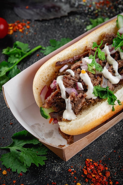 Hot dog with vegetables stuffing with chicken beef and herbs on a dark stone table The concept of fast food and delivery restaurants