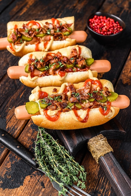 Hot dogs fully loaded with fried bacon, onion and pickled cucumbers. Dark Wooden table. Top view.