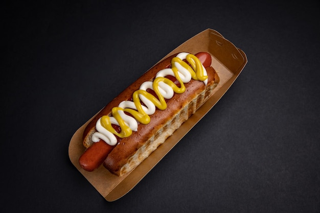 Hot dogs in paper plates with sausages and sauce on a black background