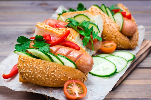 Hot dogs with sesame buns and fresh vegetables on a plate on a wooden table