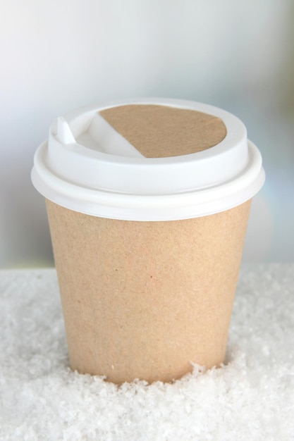 Hot drink in paper cup and snow on bright background