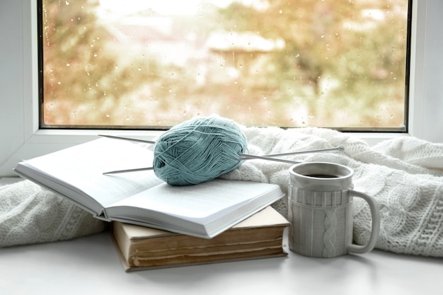 Hot drink with books, threads and plaid on windowsill