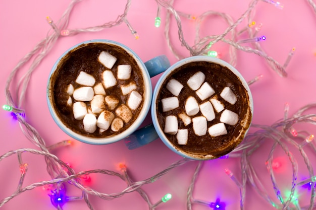 Hot drink with marshamllows in blue cups top view and shiny electric garland lights