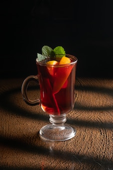 Tè caldo alla frutta con arancia, fette d'arancia, foglie di menta e una stecca di cannella in un bicchiere di vetro trasparente con manico. Foto Premium