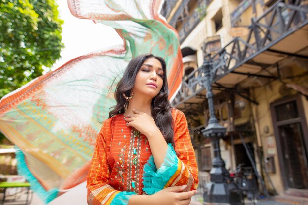 Photo hot girl closed eyes, waving dupatta wearing traditional dress at walled city lahore for photoshoot