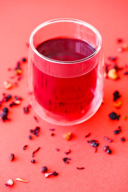 Hot hibiscus tea in a transparent glass with a double bottom on a red background. Selective focus