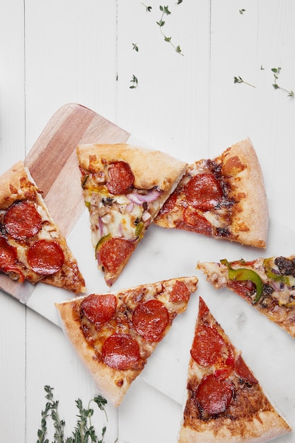 Hot Italian pizza with melting tomato,pepperoni and cheese on a white rustic wooden table.