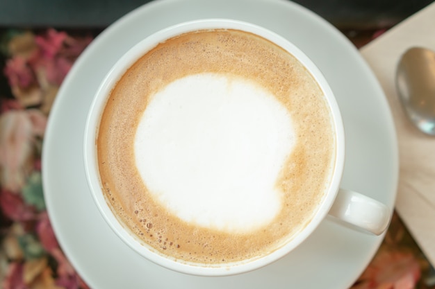 Foto il caffè caldo di arte del latte in tazza bianca con il cucchiaio del metallo ha offuscato il fondo