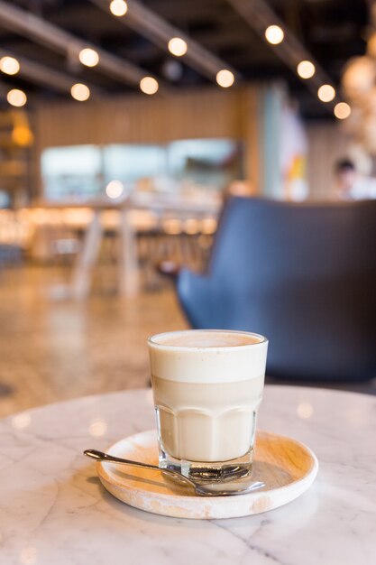 Hot latte in a glass cup with spoon and wooden plate. 