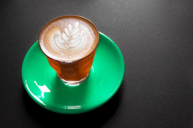 Hot latte in orange and green cup with floral pattern in foam on a dark background