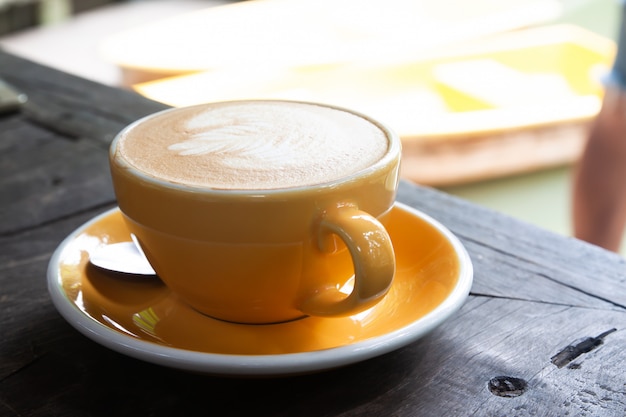 Hot latte in yellow cup on wooden table