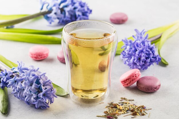 Hot lemongrass tea in a glass with double walls on a light background decorated with flowers