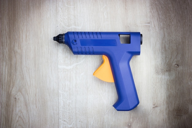 Hot-melt gun, construction tools. Melting silicone glue gun, closeup. Isolated on wooden background.