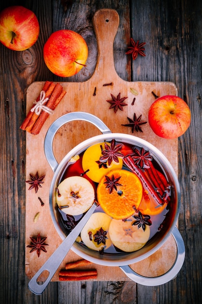 Hot mulled wine drink with citrus apples cinnamon sticks cloves and anise in cooking pan on wooden background