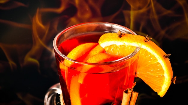 Hot mulled wine in a glass next to the burning fireplace. Hot christmas beverage. Orange slices, cinnamon sticks, anise star. Copy space. Holiday atmosphere. Christmas greeting card