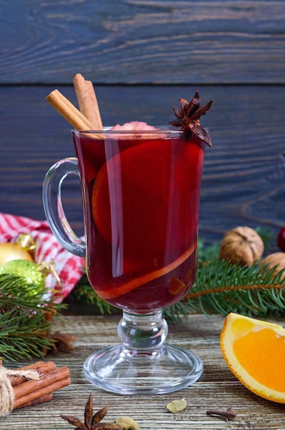 Hot mulled wine in glass mug on a wooden table. Fragrant traditional winter drink based on wine, juice, spices, seasonings, fruits. Close up