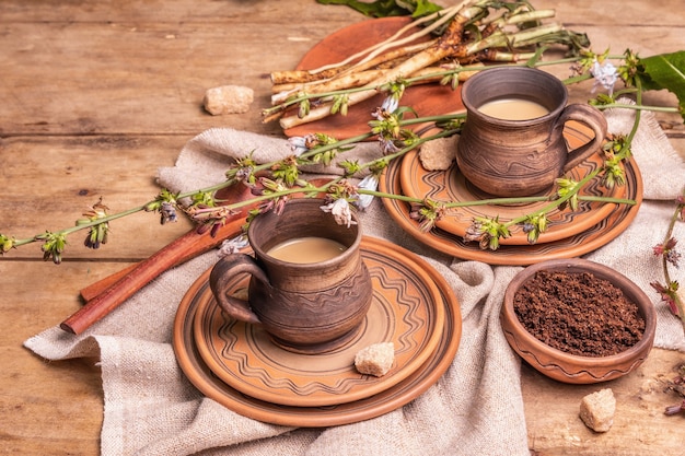 木製のテーブルの上のセラミックカップでホットナチュラルチコリカフェインフリードリンク。コーヒー、カフェインの健康的な代替品。青いチコリの花、新鮮な根、コピースペース