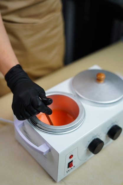 Hot orange wax used for hair removal. Close-up of depilation master hands in black protective gloves