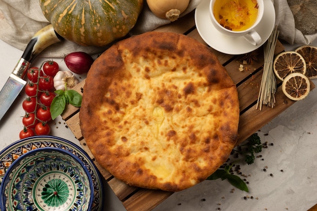 Hot Ossetian pie with pumpkin filling and herbs next to decorative national Uzbek ceramic dishes with a traditional pattern.