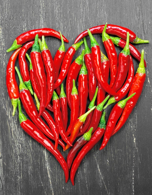 Hot peppers forming a heart on old wooden table black