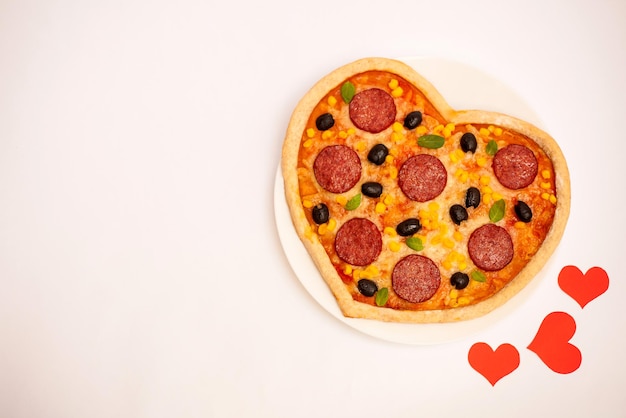 Photo hot pizza in the shape of a heart with sausage corn cheese olives on a white isolated background