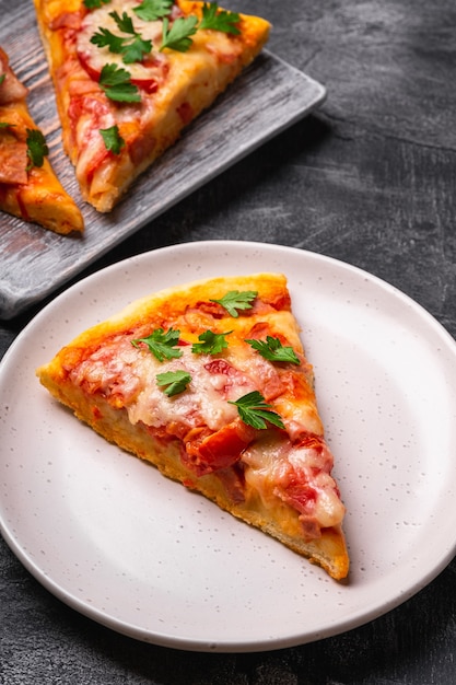 Hot pizza slices with mozzarella cheese, ham, tomato and parsley on wooden cutting board and plate