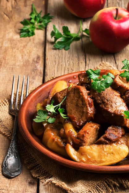 Hot pork stew with apple slice on the plate vintage wooden kitchen table background selective focus