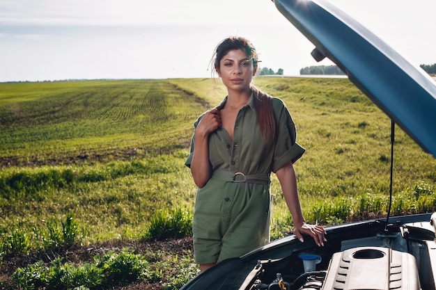 Photo hot pretty woman is holding the collar of his overalls and posing next to the open hood of her car, portrait