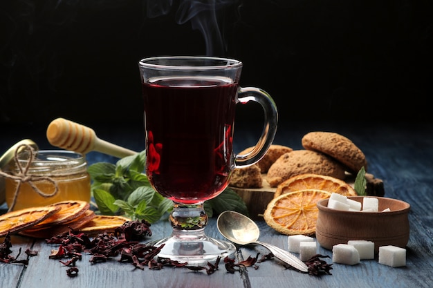 Hot red karkade tea with honey and biscuits on blue wooden table