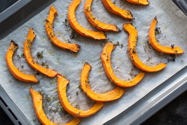 Fette di zucca arrosto a caldo con timo, olio d'oliva e sale su carta da forno. gustoso cibo vegano.