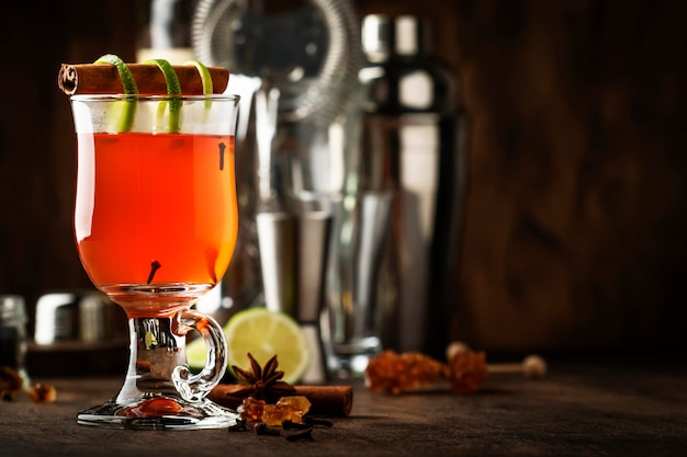 Горячий ромовый пунш грог осенний или зимний согревающий алкогольный коктейль с темным ромом, портвейном, медом, лаймовым соком, черным чаем, корицей и гвоздикой в высоком стакане на старинном деревянном фоне