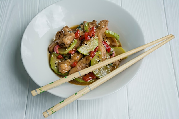 Photo hot salad with chicken, zucchini and chili pepper, sprinkled with sesame seeds and herbs. asian food. white wood .