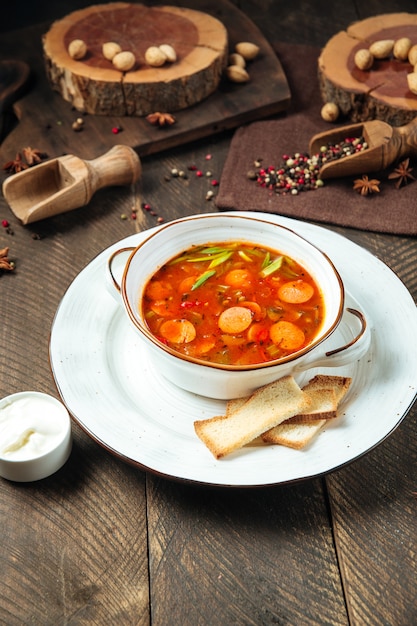 Hot sausage-tomato soup in a white bowl on the wooden table