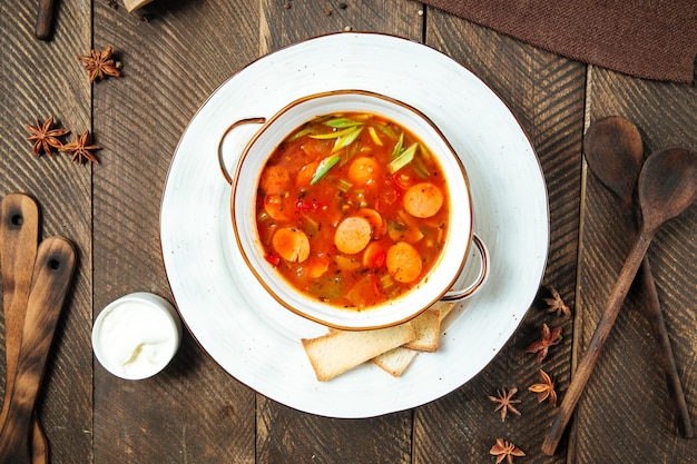 Photo hot sausage-tomato soup in a white bowl on the wooden table