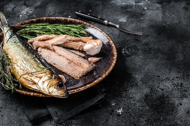 Hot Smoked herring fish fillet on rustic plate with thyme and rosemary Black background Top view Copy space