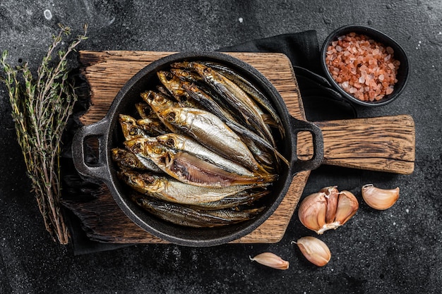 Hot Smoked sprat and Anchovy fishes in pan. Black background. Top view.