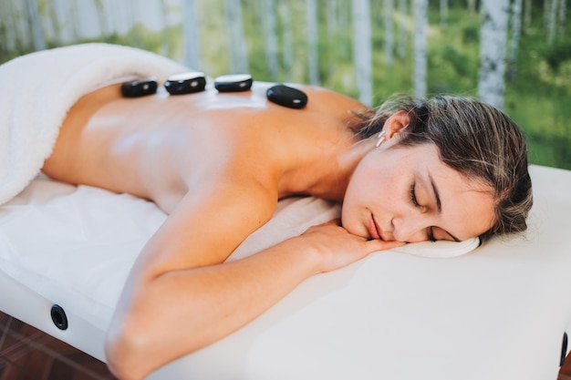 Hot spa volcanic lava stone placed on a female patient\'s back\
by a physiotherapist energy stones