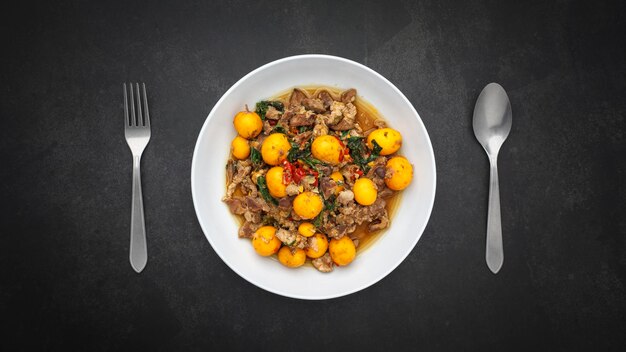 Photo hot and spicy stir fried chicken ovary egg with chicken entrails and basil beside spoon and fork