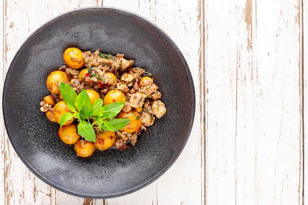 Uovo di ovaia di pollo fritto caldo e speziato con interiora di pollo cotoletta varietà di carne carni d'organo e basilico in piatto scuro su sfondo bianco struttura in legno vista dall'alto cibo di strada locale tailandese