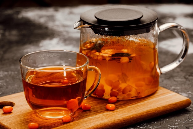 Hot spicy tea with sea buckthorn in a glass teapot and Cup on a dark background