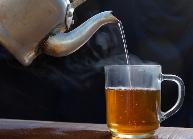 Hot tea cup has hot steam with kettle. Placed on an old wooden table, black background